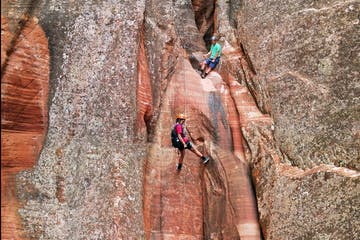 Two climbers navigate a narrow rock crevice in a rugged landscape.